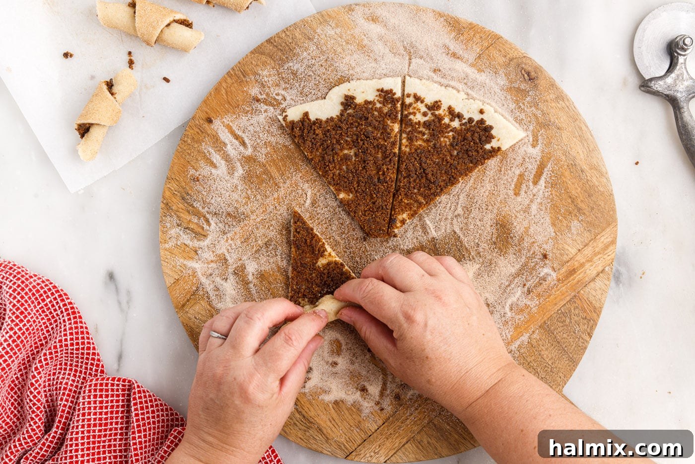 Hands demonstrating the rolling technique for rugelach, starting from the wide end and rolling inward to form a crescent shape.