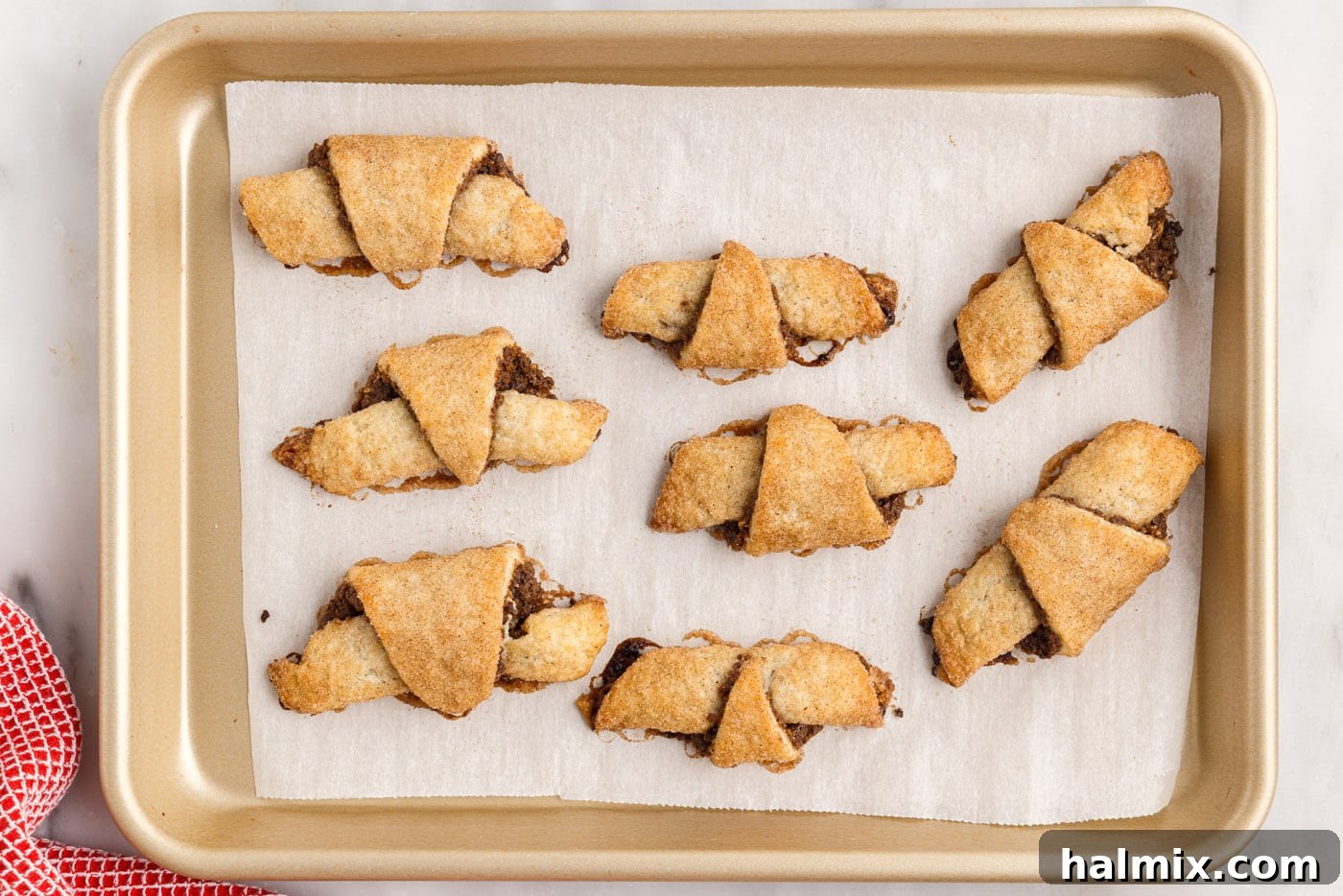 A close-up of baked cinnamon raisin rugelach, golden brown and perfectly cooked, with visible filling.