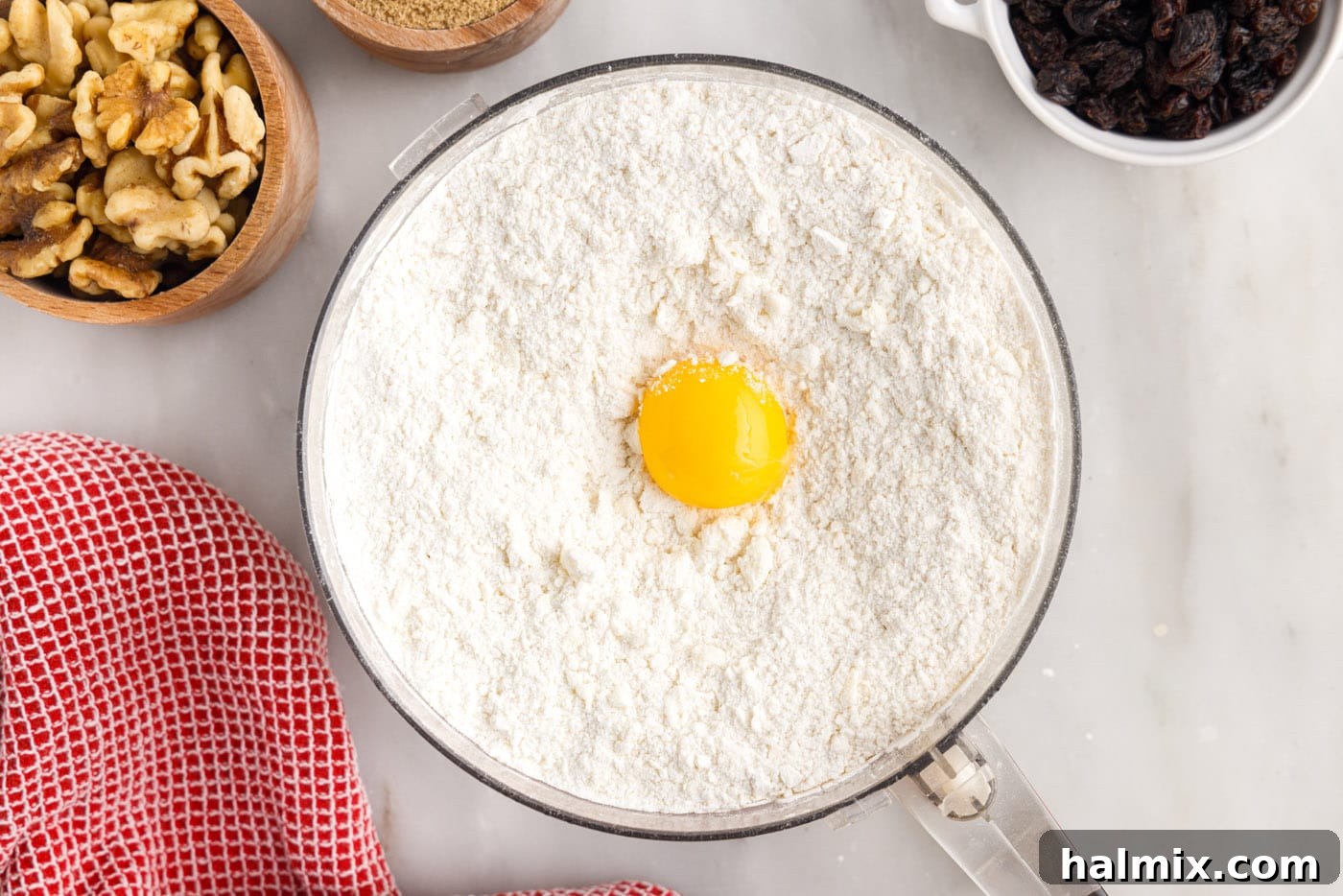 A single egg yolk rests on top of the crumbly cream cheese dough mixture in the food processor.