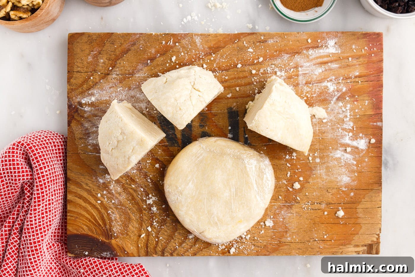 A knife is used to divide the rugelach dough ball into four equal sections on a cutting board.