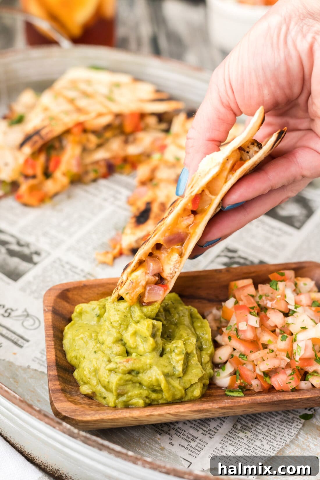 Grilled Chicken & Cheese Fiesta 12 A hand dipping a grilled chicken quesadilla triangle into a bowl of guacamole