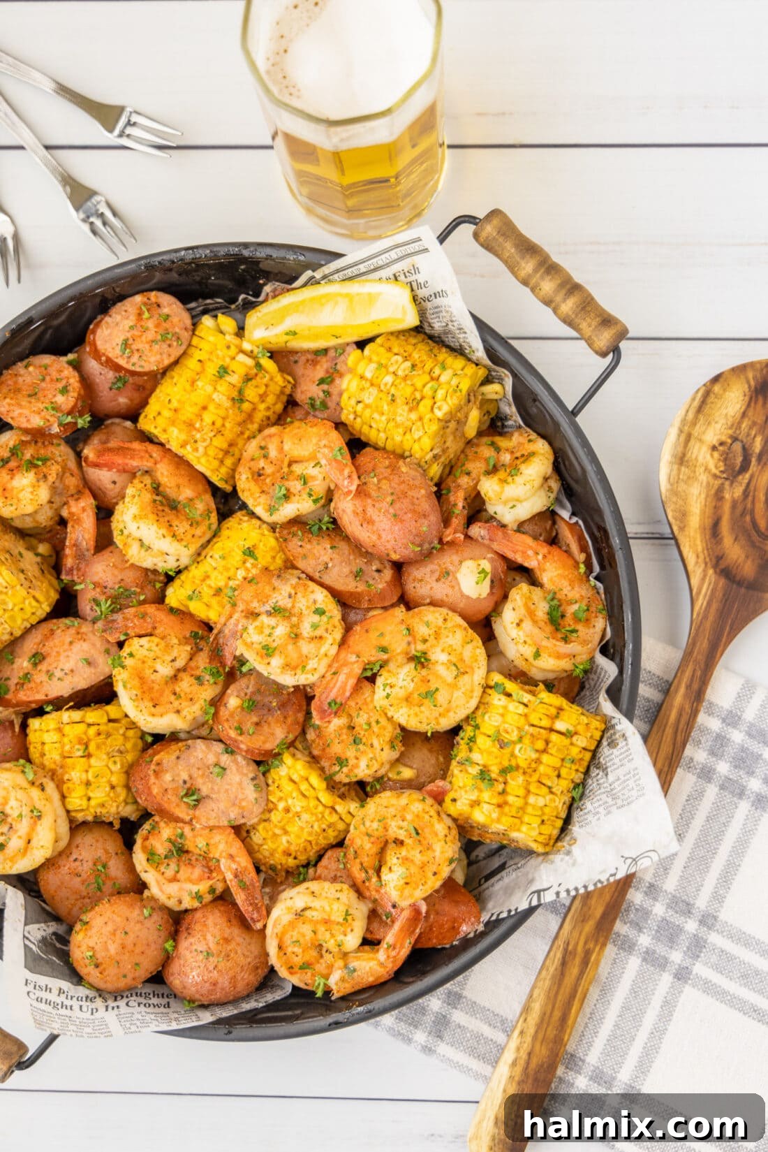 A vibrant Southern Shrimp Boil on a platter, served with refreshing beer and a spoon, showcasing succulent shrimp, sausage, corn, and potatoes.