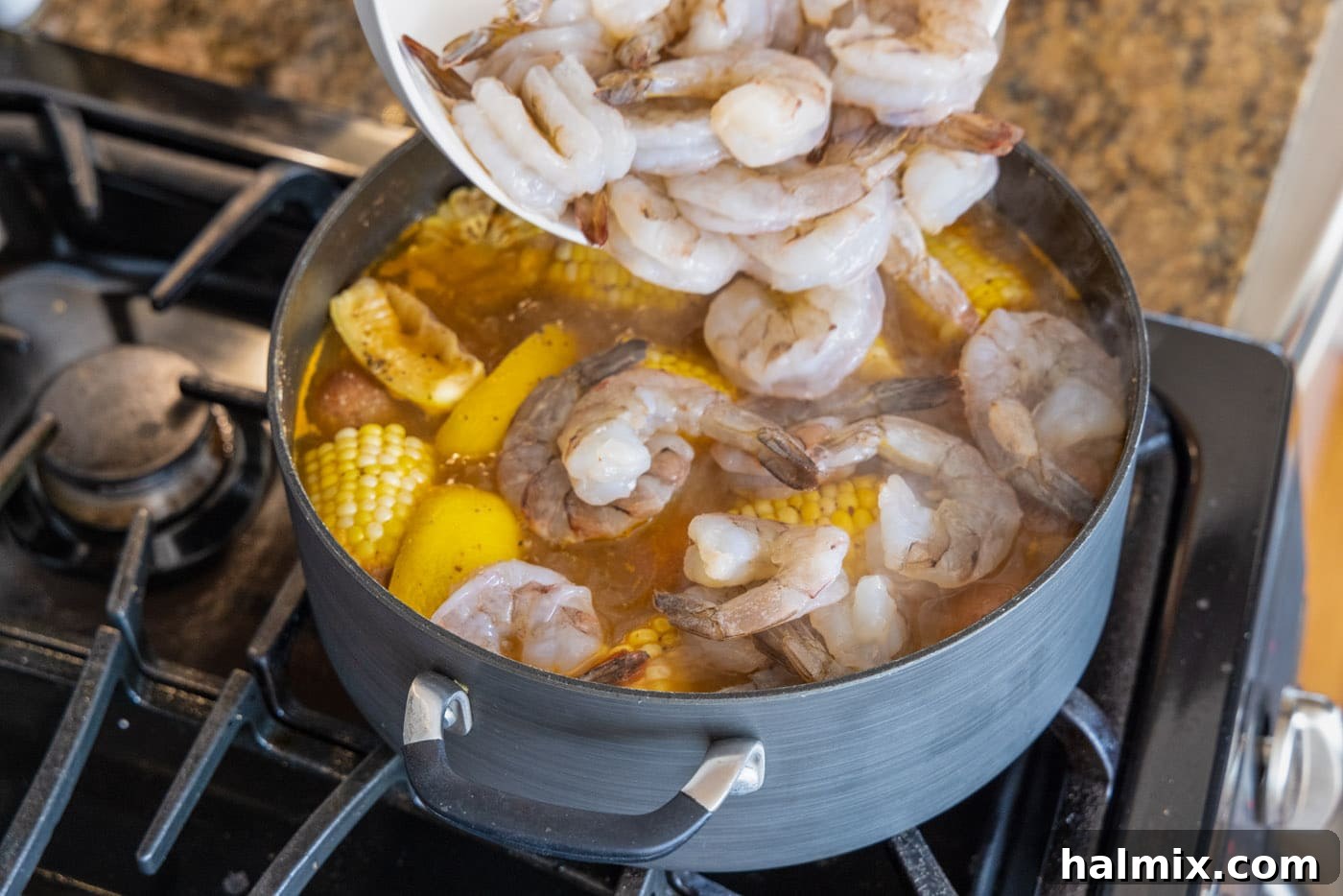 Carefully adding raw shrimp to the overflowing large pot of shrimp boil, ensuring all ingredients are combined.