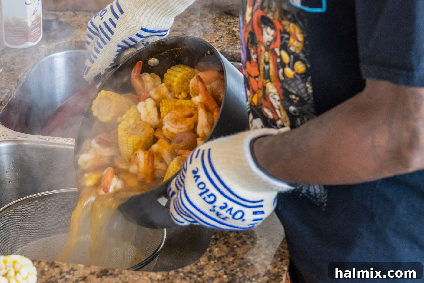 Pouring the entire shrimp boil from the pot over a colander placed in a large bowl, to separate the broth from the solid ingredients.