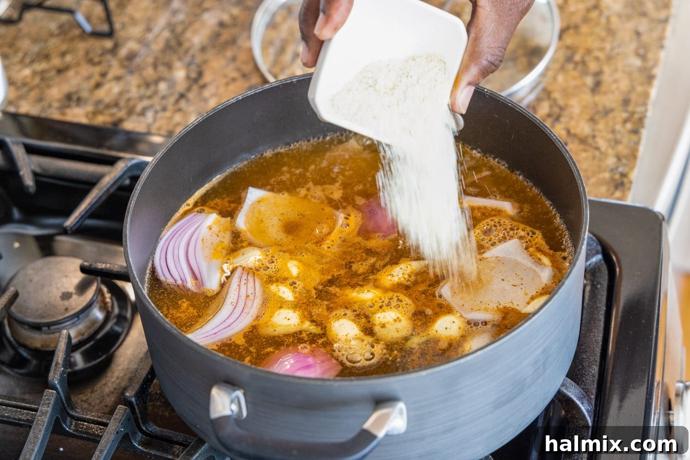Adding quartered red onions, whole garlic cloves, Old Bay seasoning, garlic salt, black pepper, and baby red potatoes to a large stockpot of boiling water.
