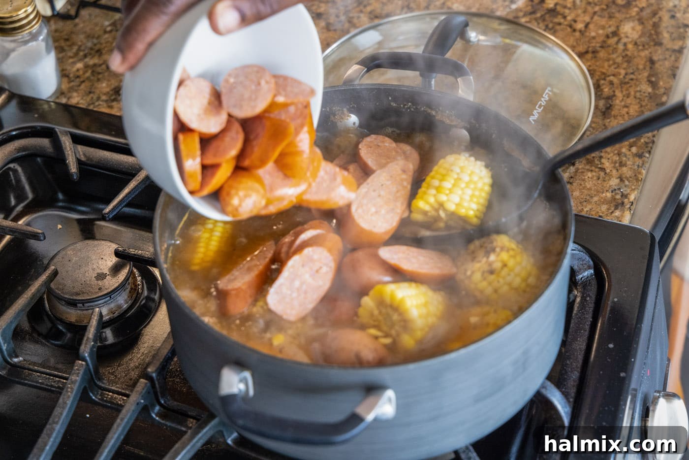 Adding sliced smoked sausage to the bubbling shrimp boil, enhancing the savory profile of the dish.