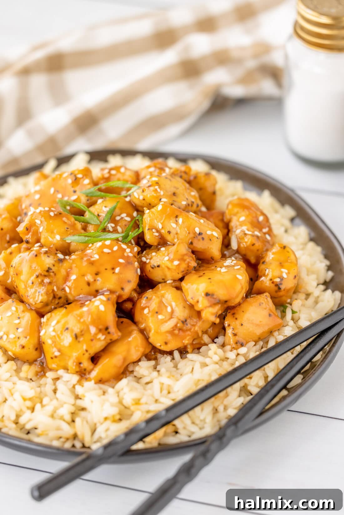 Plate of Bourbon Chicken on rice, garnished with green onions and sesame seeds