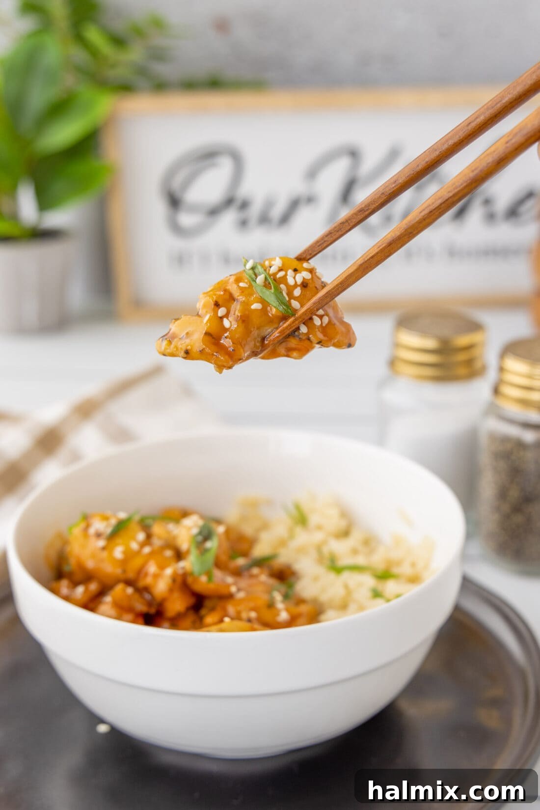 Lifting a piece of Bourbon Chicken with chopsticks from a serving bowl