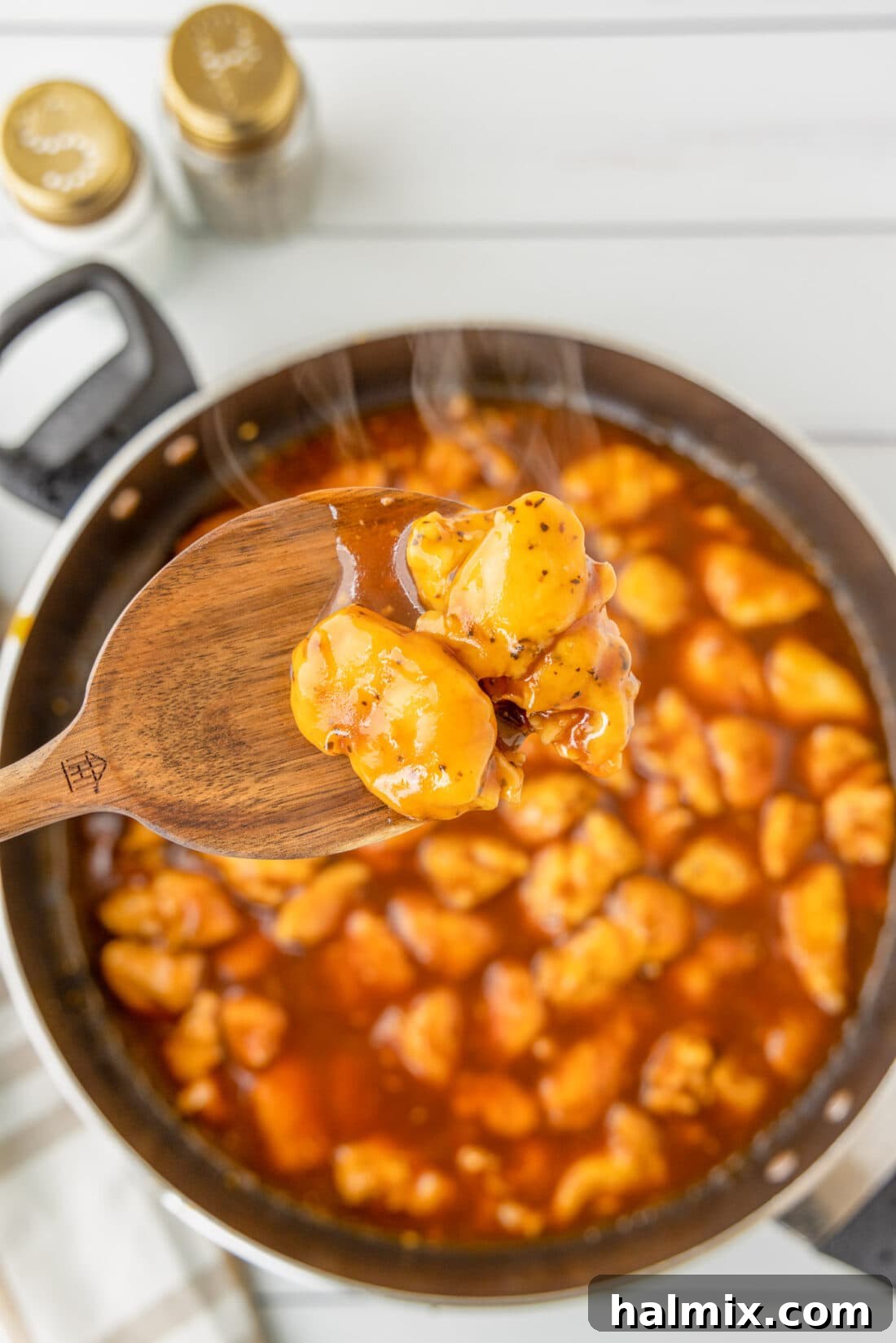Spoon lifting Bourbon Chicken from a skillet, showcasing the sticky sauce