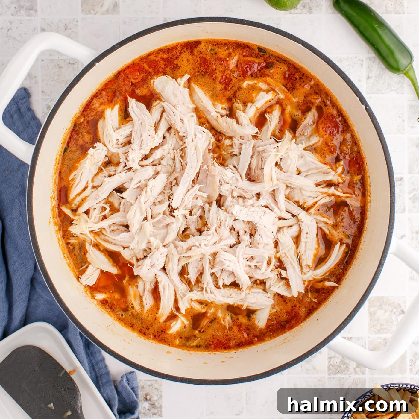 Shredded chicken being added to the simmering tortilla soup