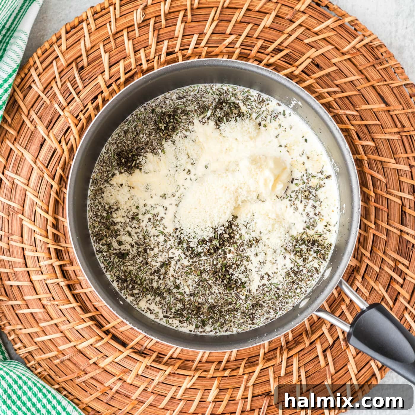 A close-up view of the ingredients for rosemary cream sauce simmering in a saucepan, including butter, garlic, rosemary, and cream, before the final thickening.