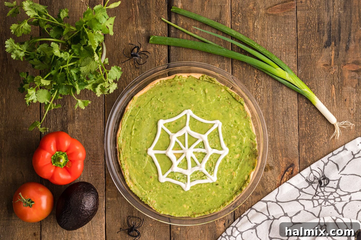 A completed sour cream spider web artfully piped on top of the guacamole layer of the taco dip, creating a striking Halloween effect.