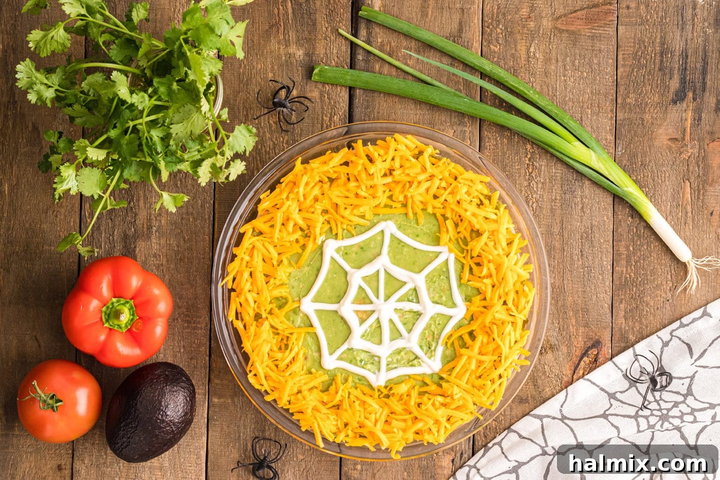 Shredded cheddar cheese sprinkled around the perimeter of the pie plate, bordering the sour cream spider web on the taco dip.
