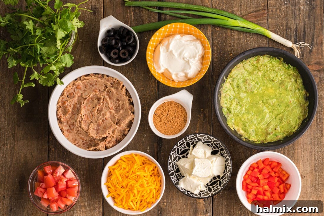 A colorful array of fresh ingredients for Spider Web Taco Dip laid out on a kitchen counter, including sour cream, cream cheese, taco seasoning, guacamole, diced tomatoes, black olives, and cilantro.