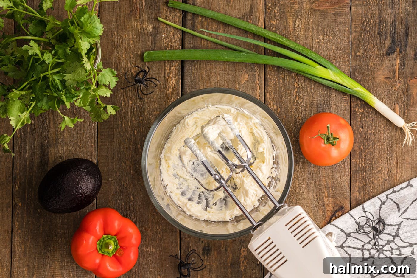 A hand mixer blending softened cream cheese in a bowl until smooth, preparing for the next layer of the dip.