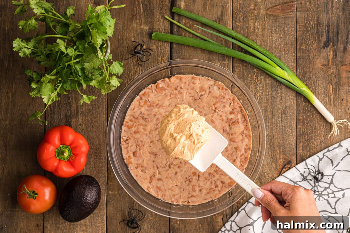 The creamy taco dip layer being meticulously spread over the refried beans, ensuring an even coat.