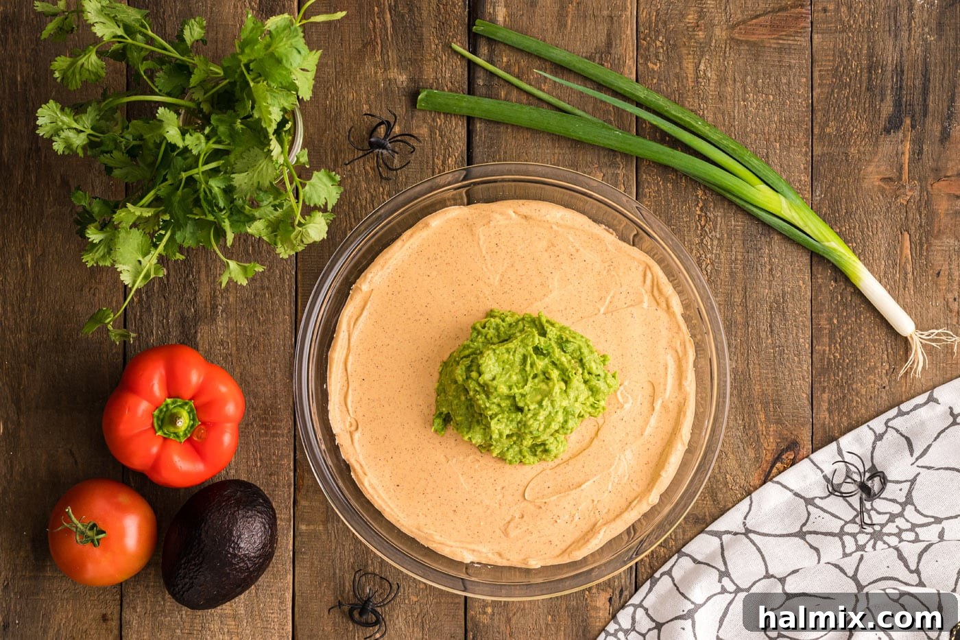 Fresh guacamole being carefully spread over the creamy sour cream and cream cheese layer, forming a vibrant green topping for the taco dip.