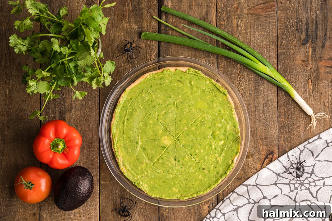 A smooth, even layer of bright green guacamole covering the entire surface of the taco dip, ready for the spider web design.