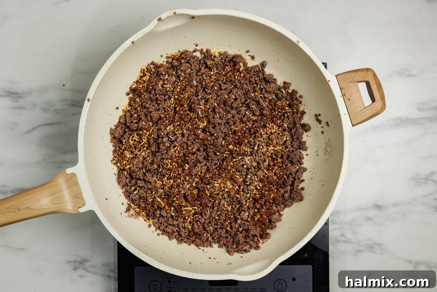 Ground beef browned in a skillet with taco seasoning and water, simmering.