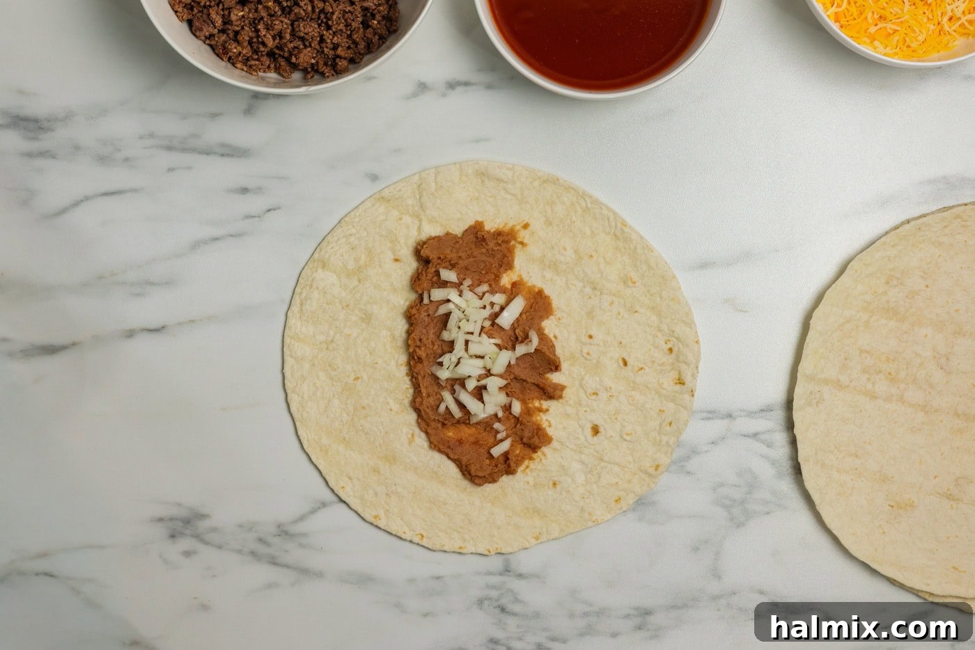 Diced onion sprinkled on top of refried beans on a tortilla.