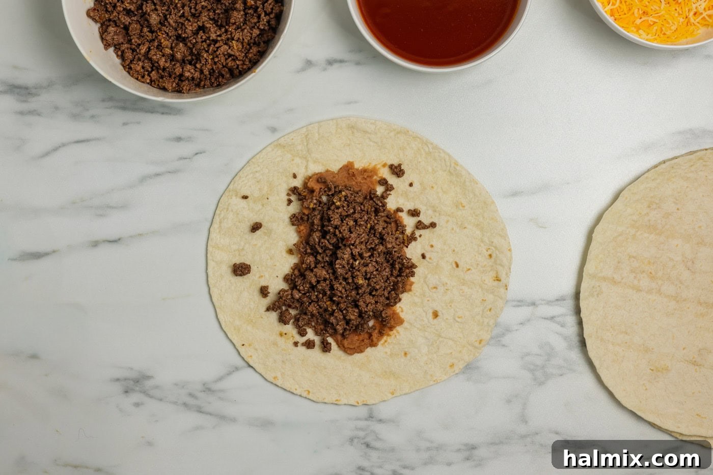 Seasoned ground beef layered over refried beans and diced onion on a tortilla.