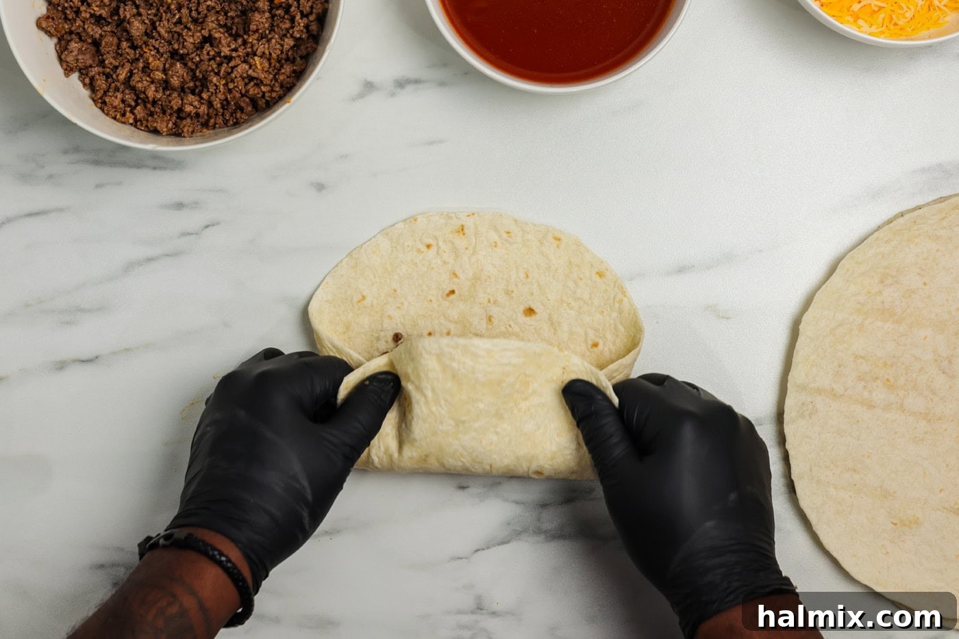 A hand rolling a tortilla burrito style with fillings, followed by enchiritos in a baking pan topped with sauce.