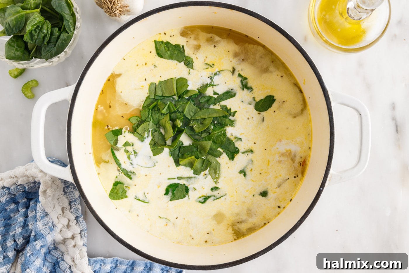 Heavy cream being stirred into the chicken gnocchi soup with wilted spinach, creating a rich, creamy texture.