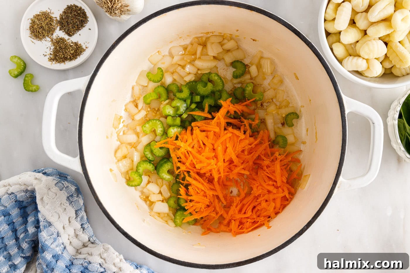 Shredded carrots and sliced celery added to the sautéed onion and garlic in a stockpot.