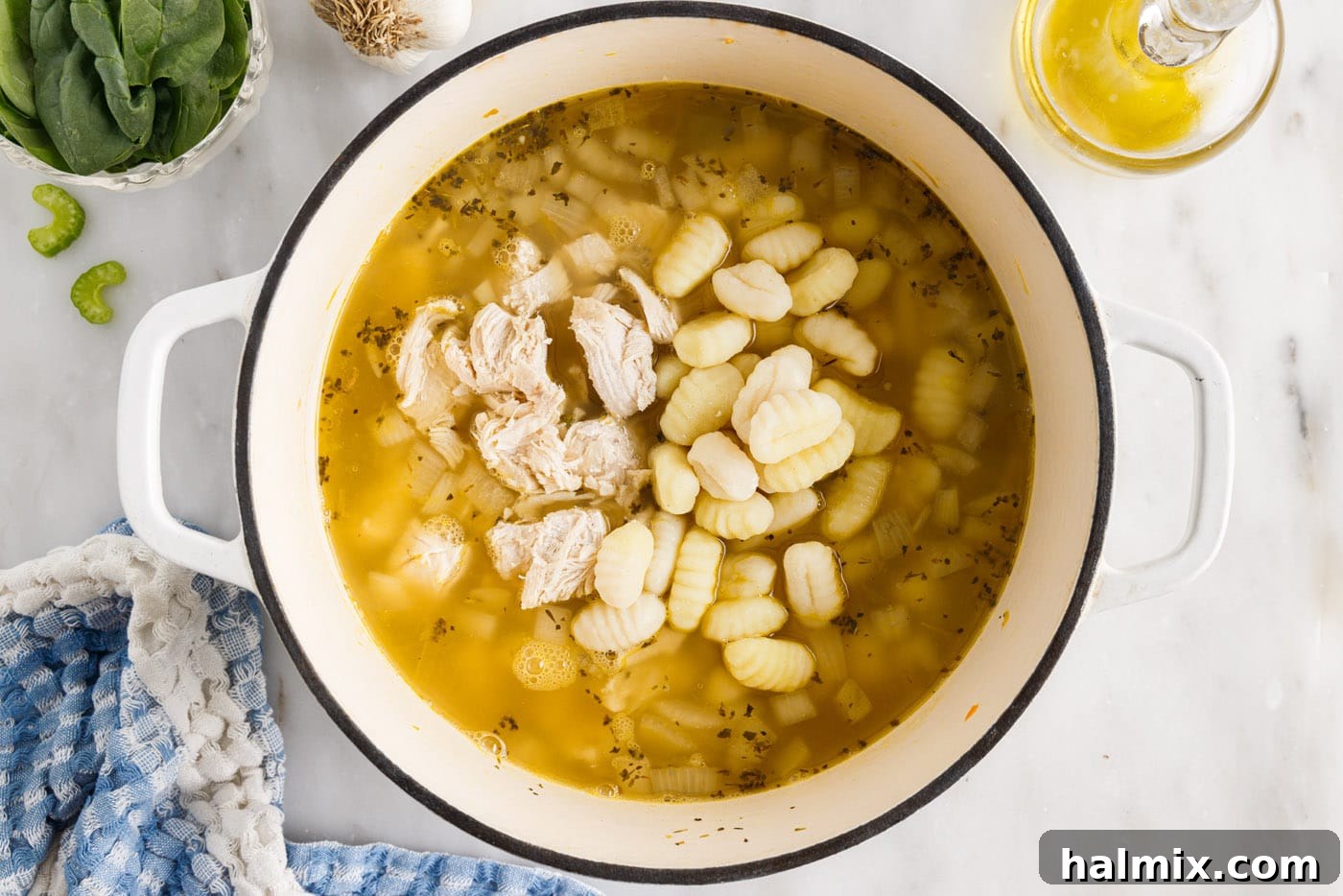 Cooked chicken pieces and gnocchi added to the simmering broth and vegetables in the soup pot.