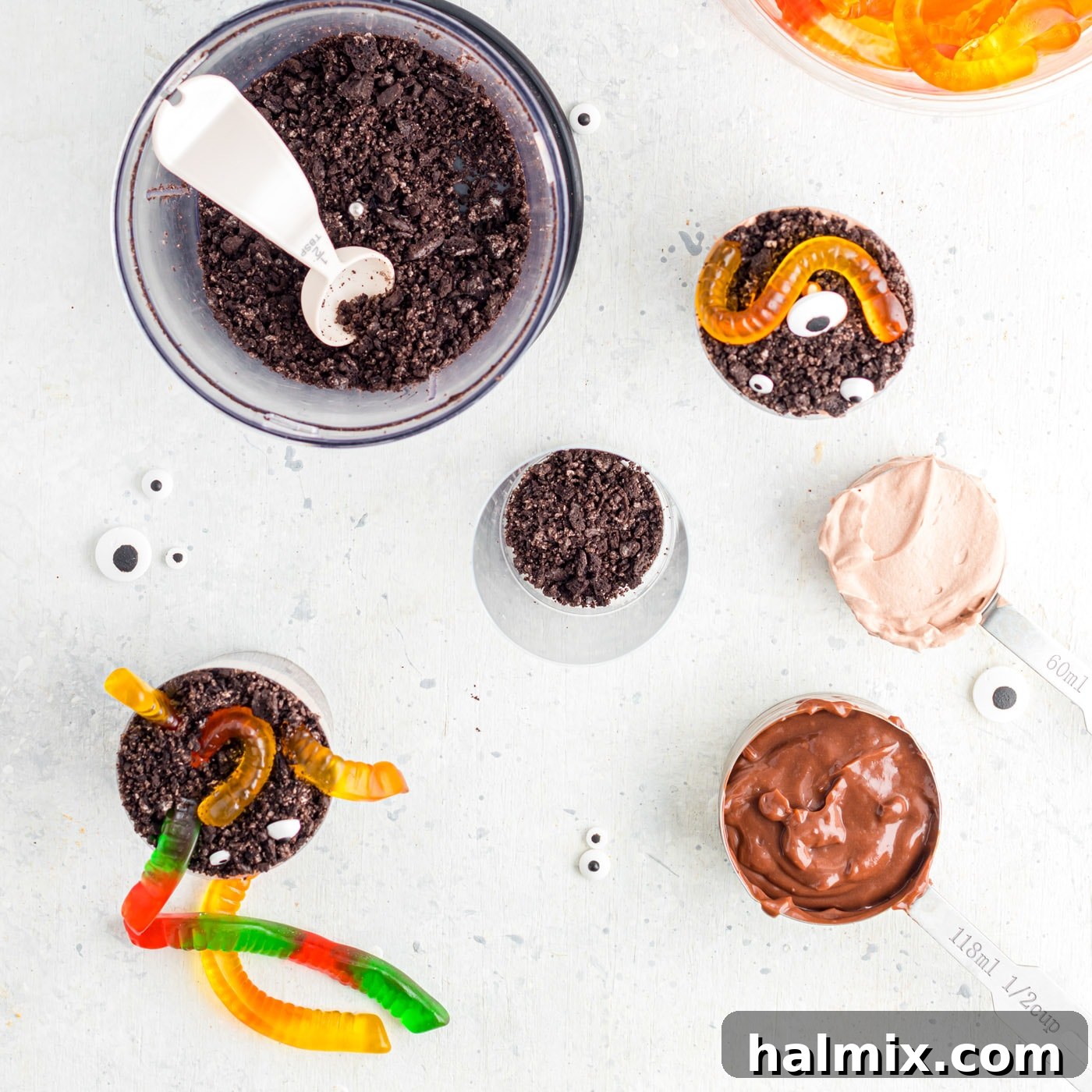 A neatly organized assembly station for Halloween Dirt Cups, featuring plastic cups, pudding, crushed Oreos, and toppings.