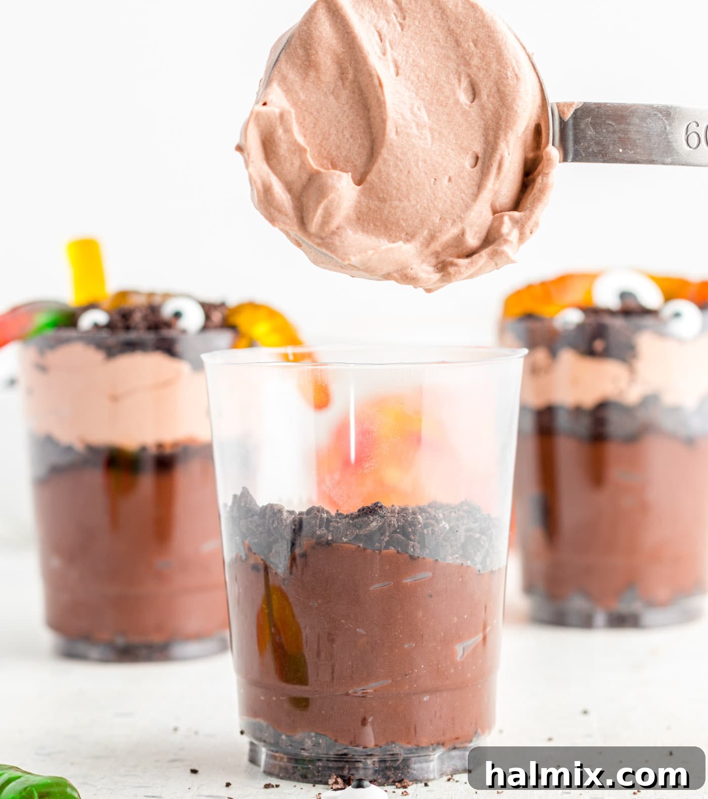 A layer of creamy whipped chocolate pudding being added over crushed Oreo cookies in a clear dessert cup.