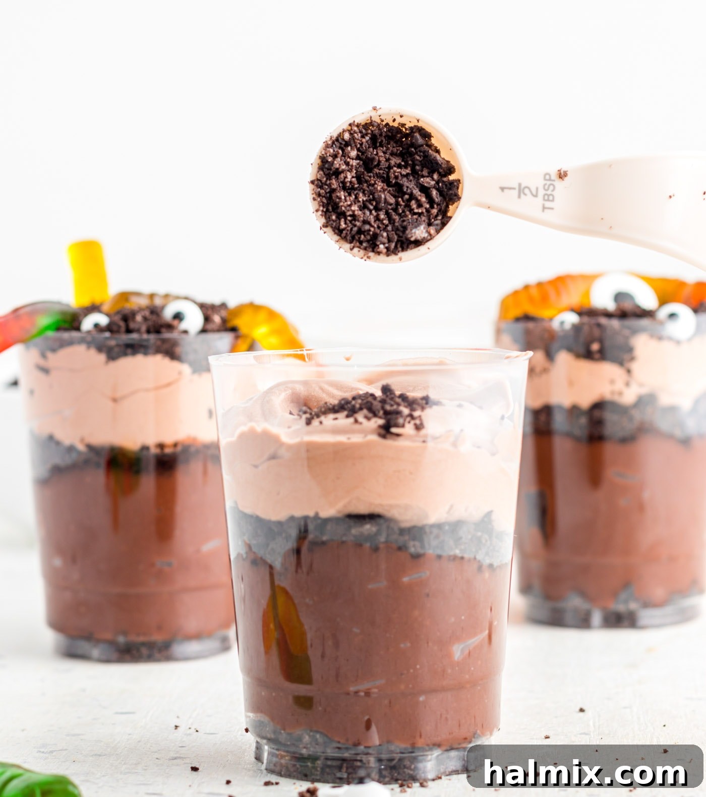 The final layer of Oreo cookie crumbs being sprinkled onto the top of Halloween dirt cups before decoration.