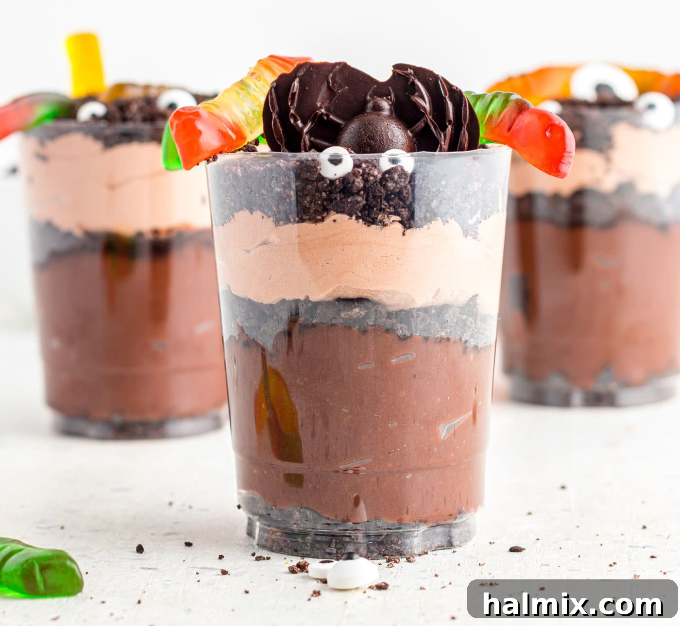 A collection of fully decorated Halloween dirt cups, each featuring gummy worms and candy, ready for a party.