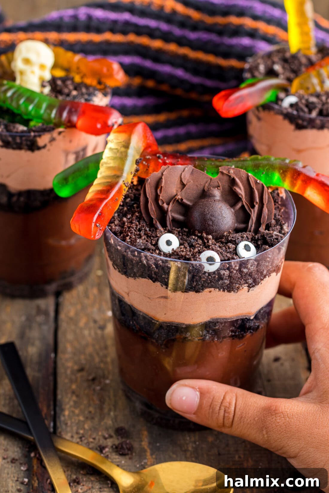 A hand reaching for a finished Halloween Dirt Cup, highlighting its readiness to be enjoyed.