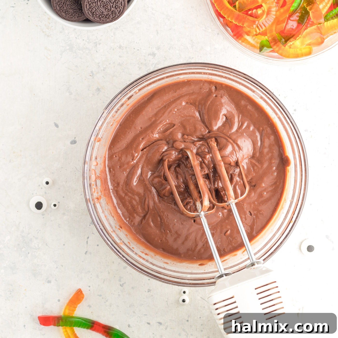 An electric mixer actively blending chocolate pudding, demonstrating the thickening process in a bowl.