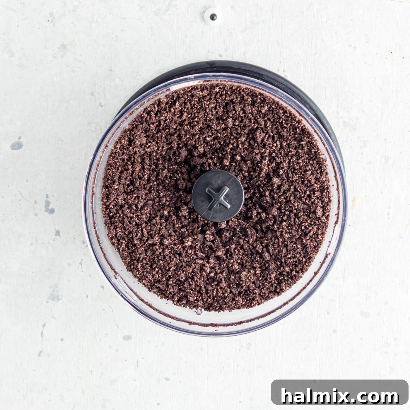 Finely crushed Oreo cookie crumbs visible inside a food processor, resembling dark, rich soil.
