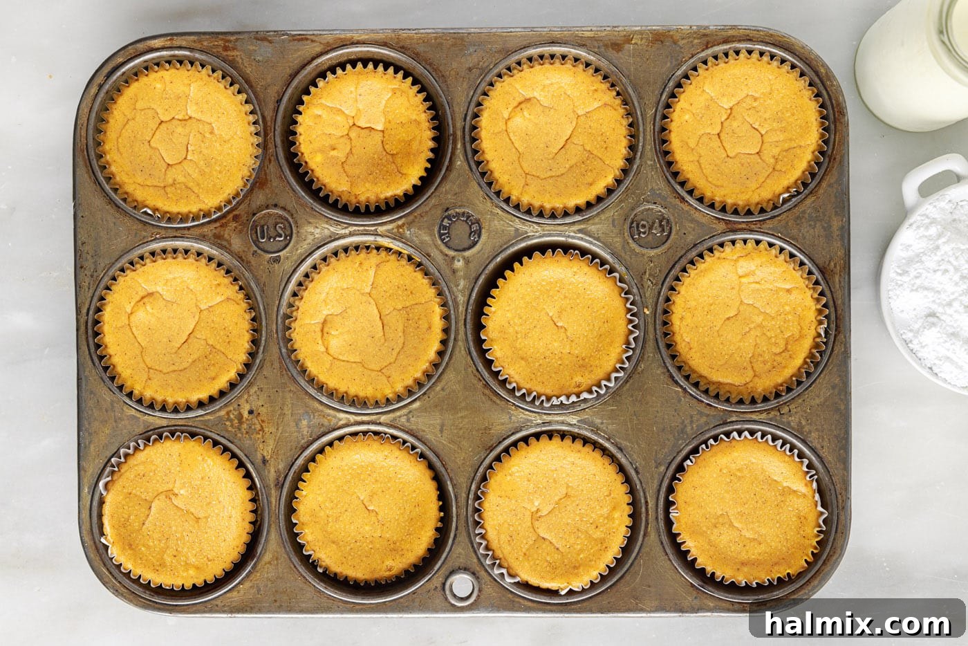 Spiced Pumpkin Cheesecake Minis 12 Mini pumpkin cheesecakes baking in a muffin tin, showing their golden tops.