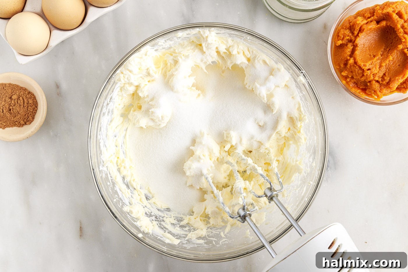 Spiced Pumpkin Cheesecake Minis 8 Cream cheese and sugar being beaten together in a large bowl with an electric mixer.