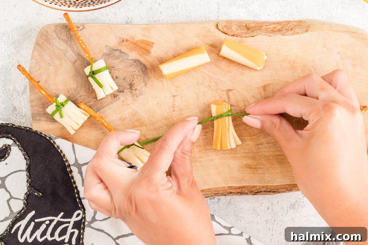 Cheesy Pretzel Broomsticks 7 A fresh chive being tied around the base of the sliced string cheese to secure the broom bristles.