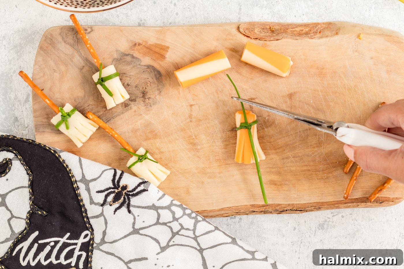 Cheesy Pretzel Broomsticks 9 Scissors trimming the excess ends of a chive after it has been tied around a cheese broomstick.