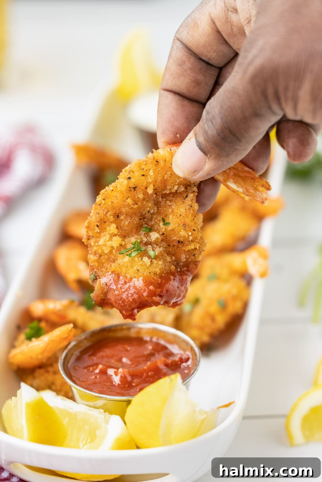 Hand dipping a crispy Butterfly Shrimp into a bowl of cocktail sauce