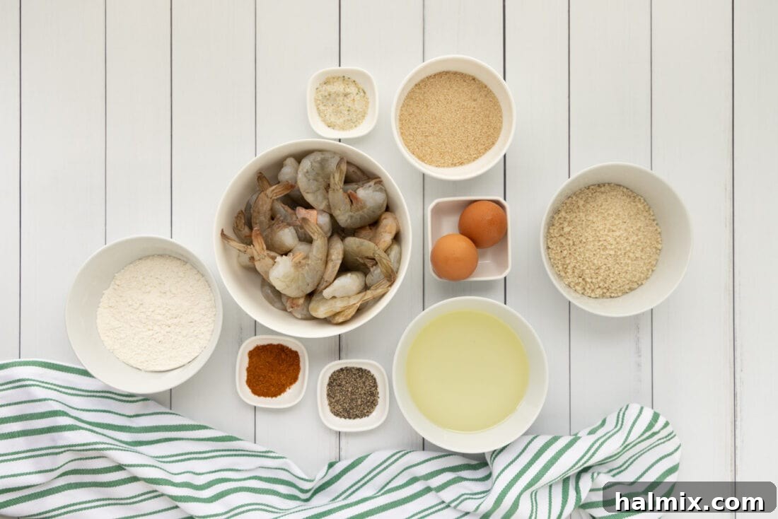 Arrangement of ingredients for making Butterfly Shrimp, including raw shrimp, bowls of flour, egg wash, and breading mixture
