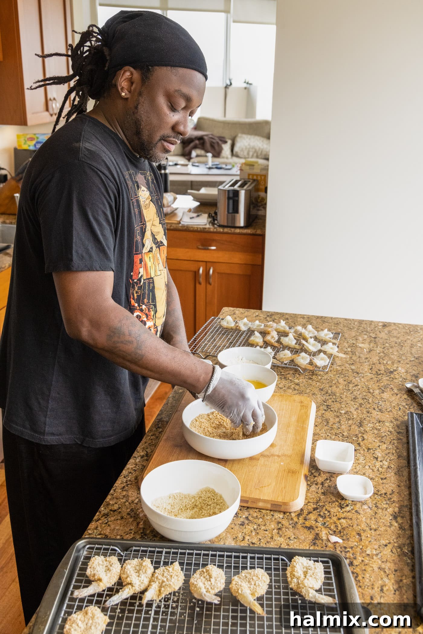 Man dredging a shrimp in a bowl of breadcrumbs and eggs