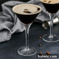 A close-up view of a frothy Espresso Martini in a martini glass, garnished with three coffee beans.