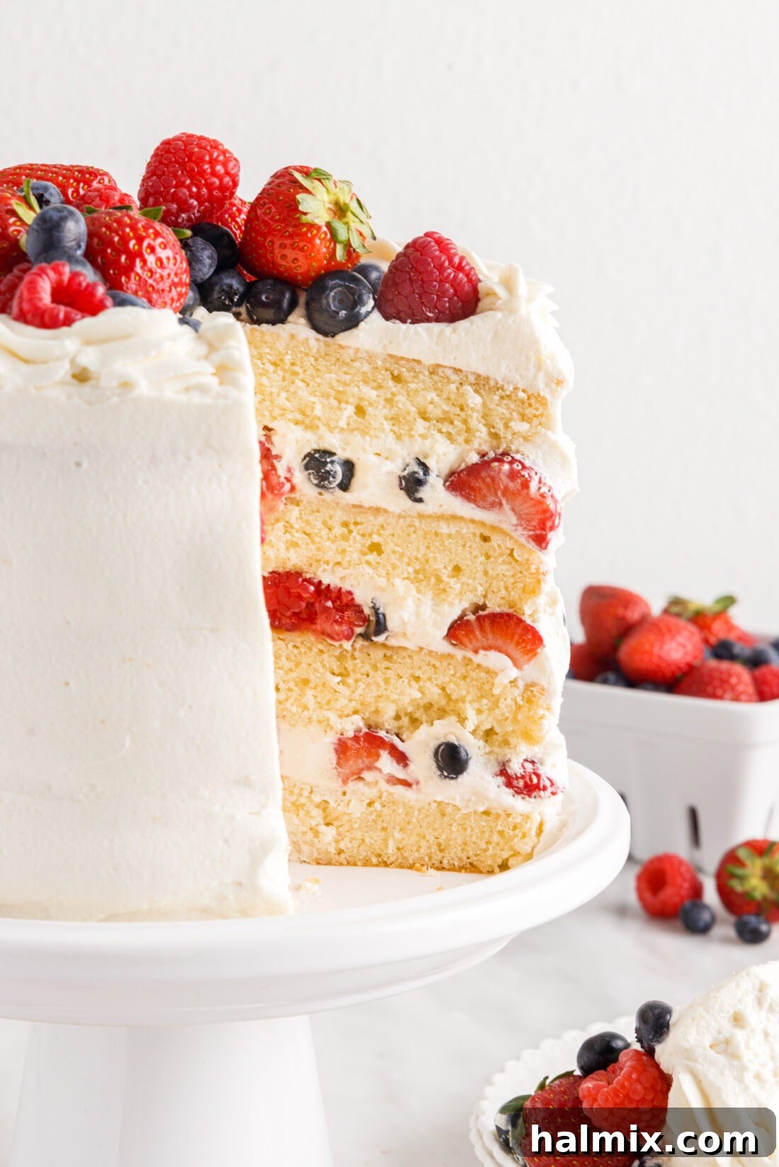 Side view of a beautifully frosted Chantilly Cake with visible layers of cake, berries, and cream.