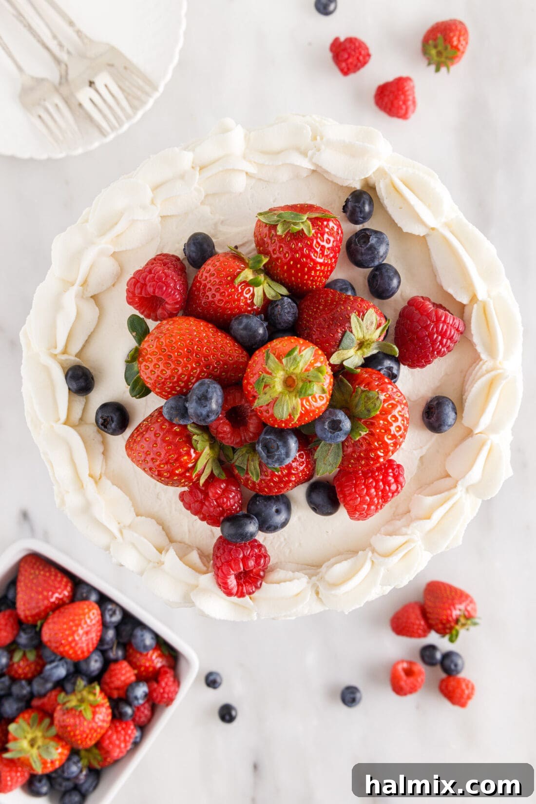 Top view of a decadent Chantilly Cake, generously adorned with fresh strawberries, blueberries, and raspberries, showcasing its vibrant appeal.