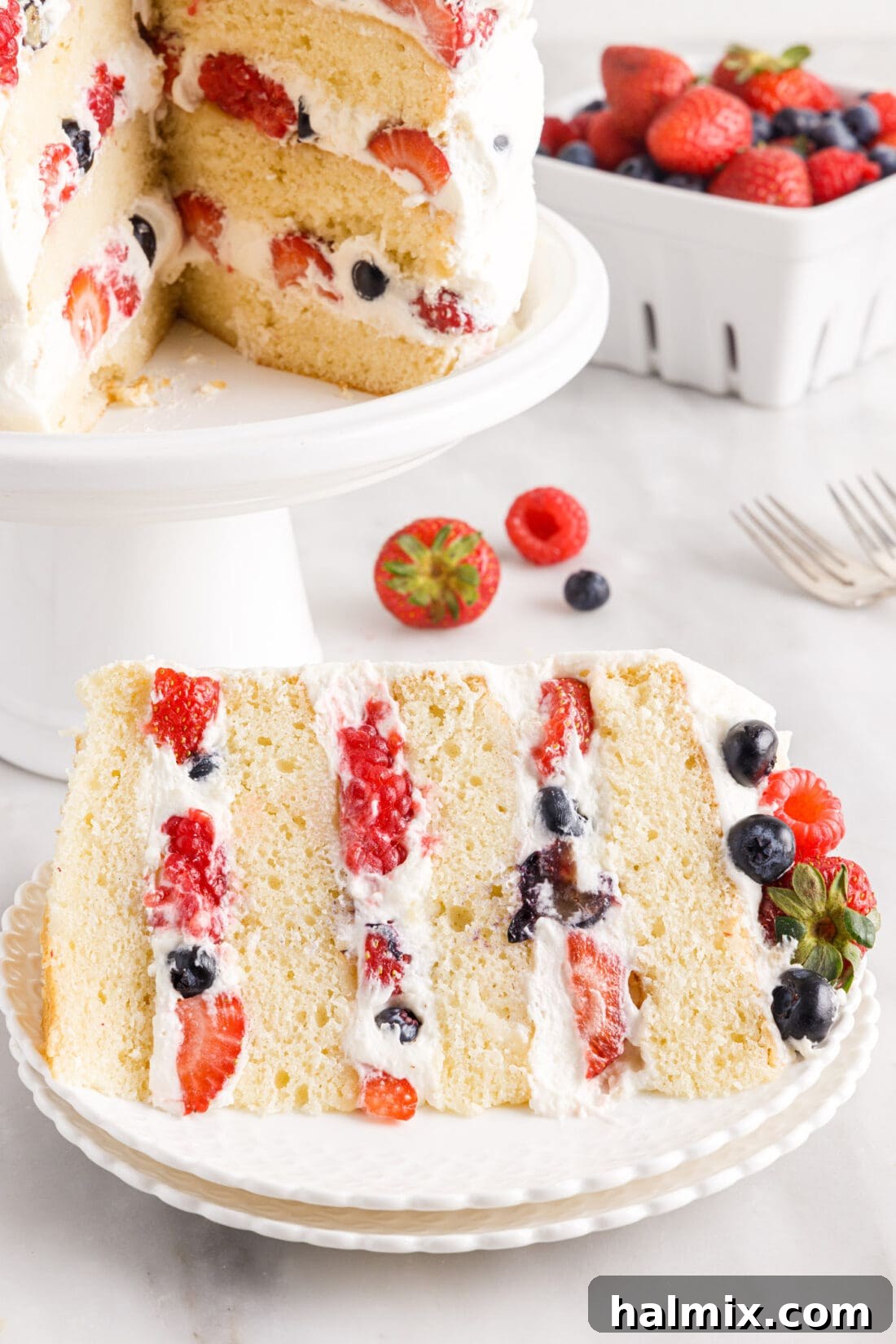 A perfectly sliced piece of Chantilly Cake revealing vibrant layers of vanilla cake, fresh berries, and fluffy frosting.