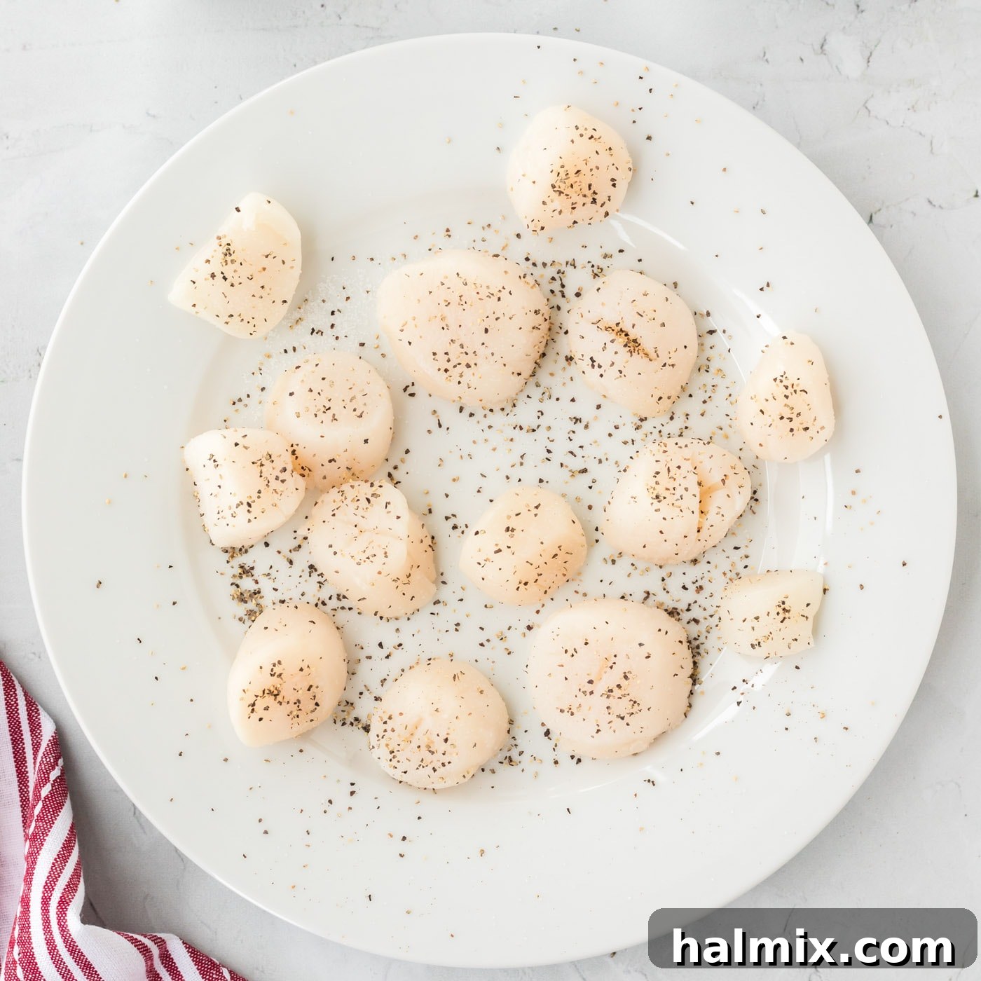 Raw scallops seasoned with salt and black pepper, laid out on a cutting board