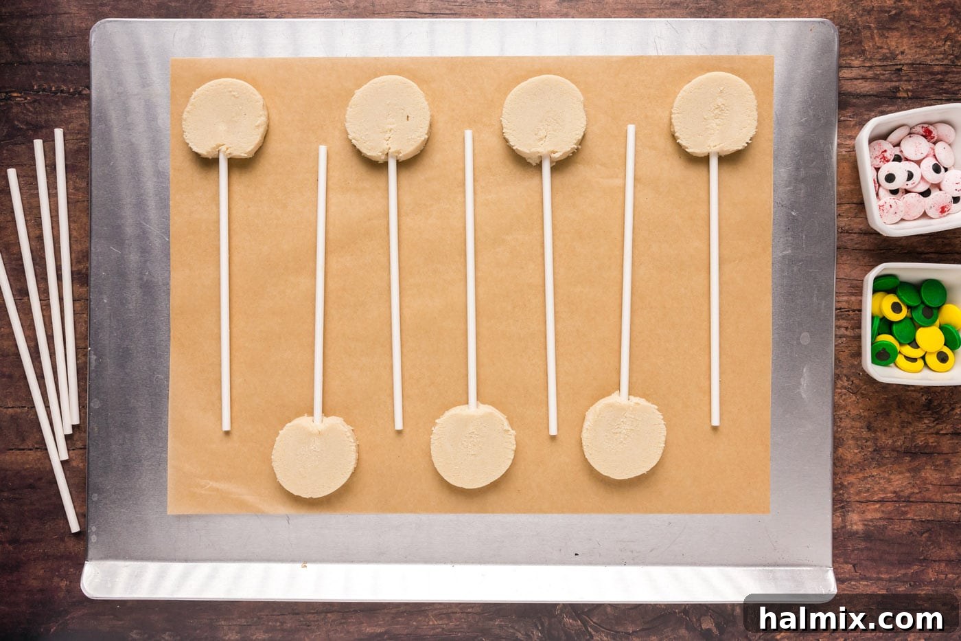 Cookie dough slices with lollipop sticks inserted on a baking sheet