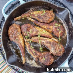 A close-up view of perfectly pan-seared Lollipop Lamb Chops resting in a skillet, showcasing their golden-brown crust and juicy appearance.
